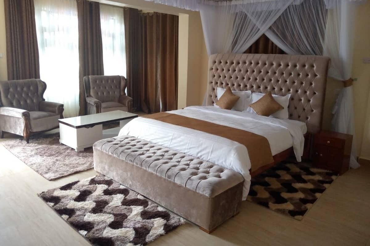 A spacious bedroom with a large bed, two armchairs, a small table, and a decorative rug.
