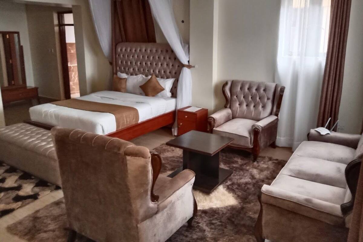 A hotel room with a large bed, a sofa, a chair, and a small table.