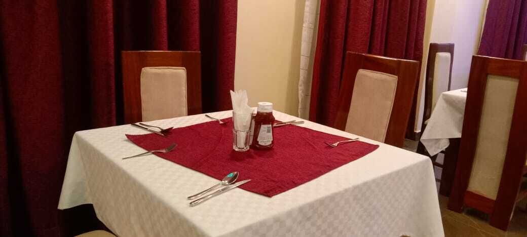 A table set with a white tablecloth, red placemat, and basic tableware including a knife, fork, spoon, and a bottle of water.