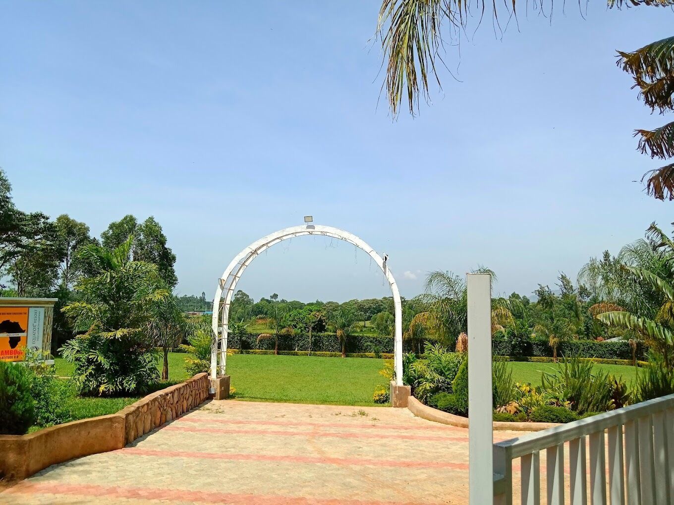 A pathway leading to a white archway in a landscaped garden with greenery and a clear sky.