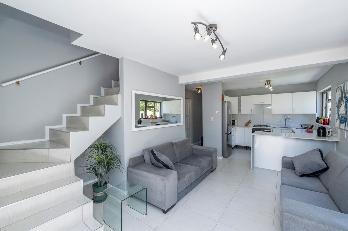 A modern living room with a grey sofa, a glass coffee table, and a staircase leading to another level.