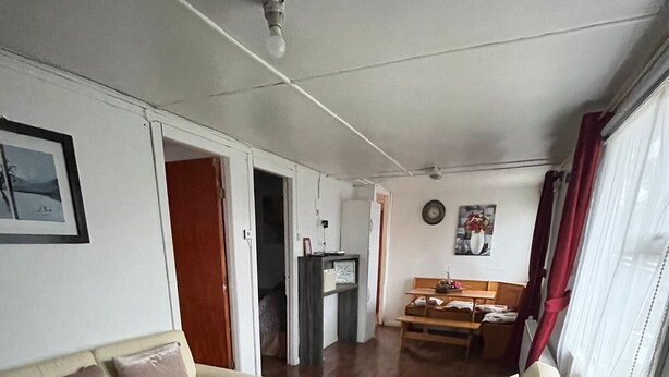 Un salon avec deux canapés de couleur crème, une table basse en bois et un tapis gris. On y trouve également un coin repas avec une table et des chaises en bois, et une cuisine visible au fond.