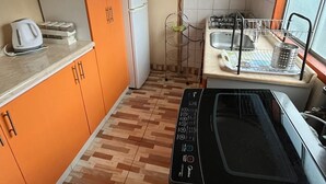 Une cuisine de taille réduite avec des meubles de couleur orange, un réfrigérateur blanc, une cuisinière à gaz et un lave-vaisselle.