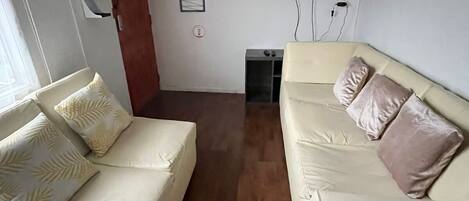 Una sala de estar con dos sofás color crema, un televisor de pantalla plana montado en la pared y piso de madera.