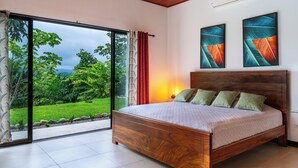 A bedroom with a wooden bed, a view of greenery, and two abstract paintings on the wall.