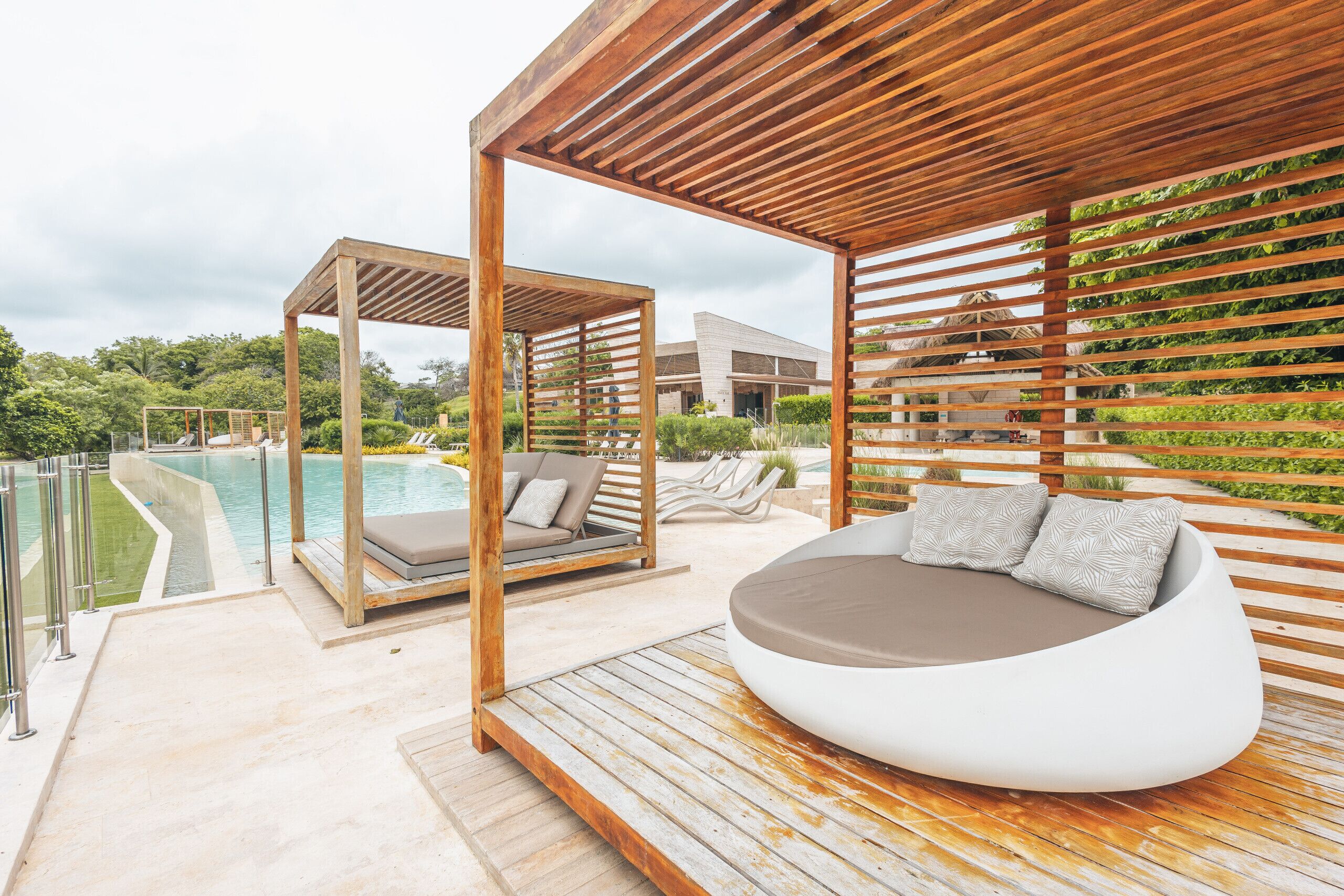 Una zona d'estar a l'aire lliure i moderna, amb una pèrgola de fusta, un seient circular i una piscina de fons.