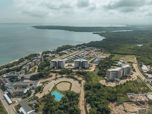 An aerial view of a coastal residential area with multiple high-rise buildings, a swimming pool, and a road network.