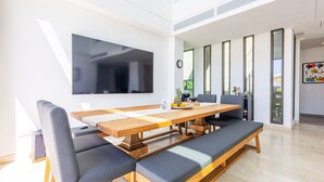 Ein zeitgemäßer Essbereich mit einem langen Holztisch, gepolsterten Bänken und einem großen Flachbildfernseher an der Wand.