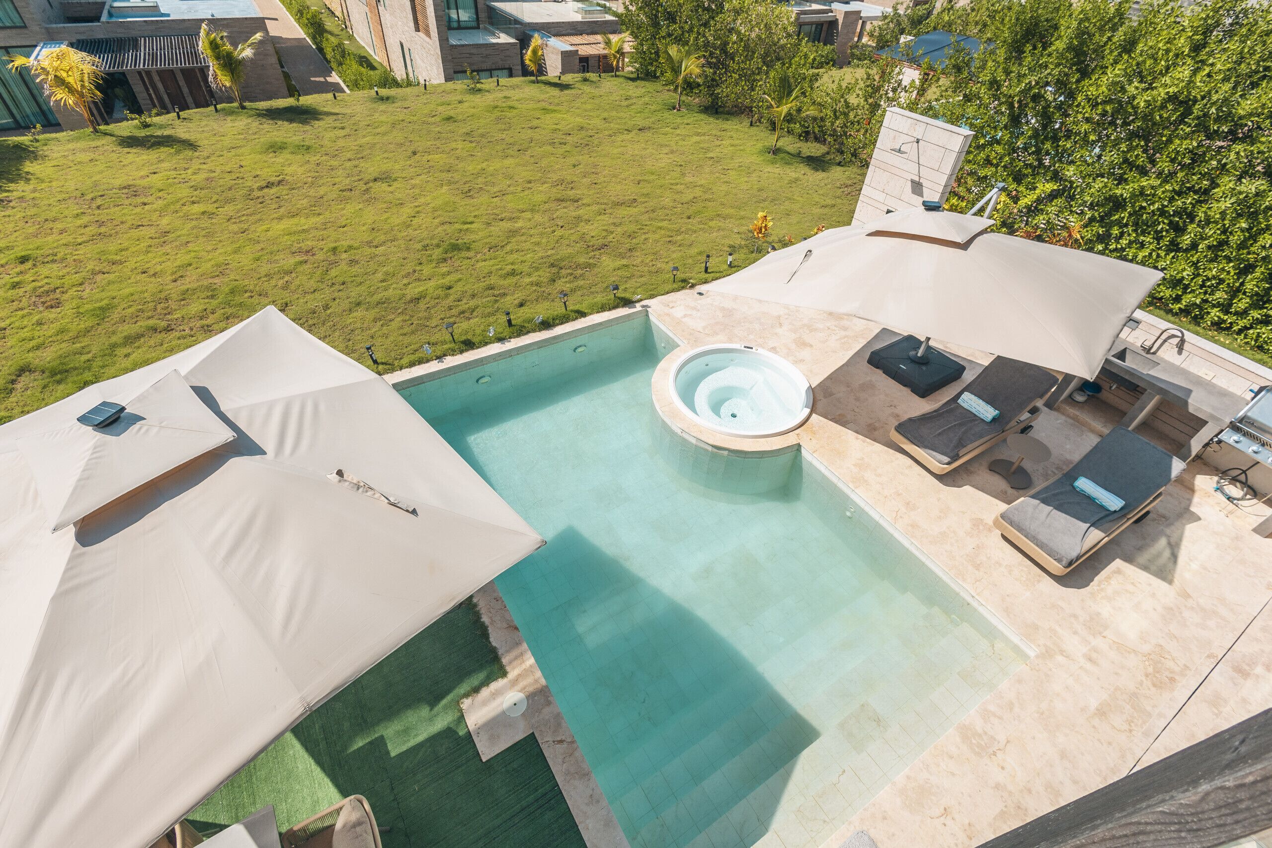 A rooftop pool with a hot tub, lounge chairs, and a grassy area with trees.
