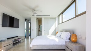 Ein modernes Schlafzimmer mit einem großen Bett, einem an der Wand montierten Fernseher und einem Deckenventilator.