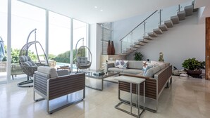 A spacious living area with a modern sofa, two armchairs, a coffee table, and a staircase leading to an upper level.