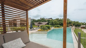 A poolside area with a wooden pergola, a cushioned seating area with a patterned pillow, and a view of a pool and surrounding greenery. - Coastal Villa w Dock Access Pools (Cartagena)