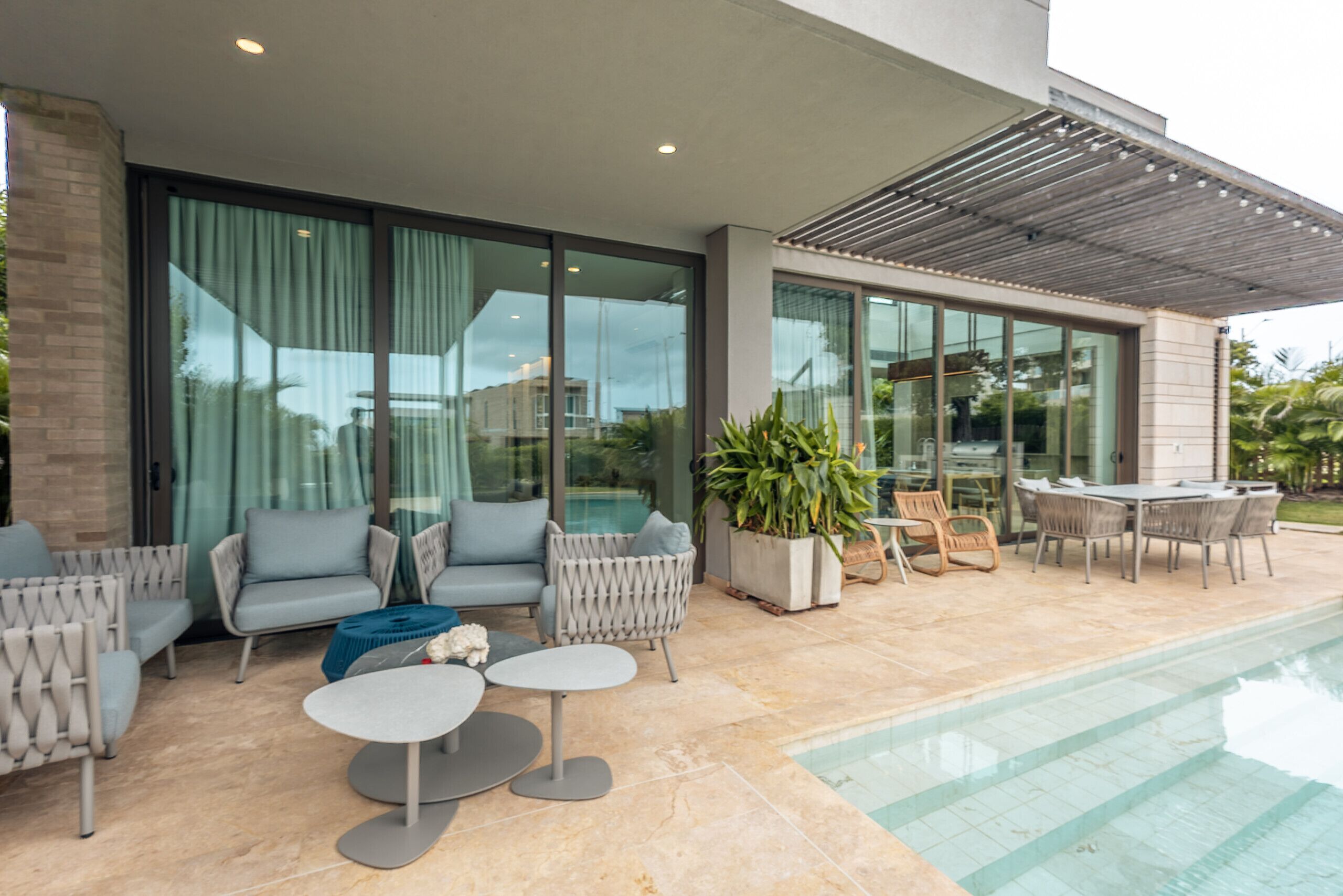 A modern outdoor patio with a pool, seating area, and large windows.