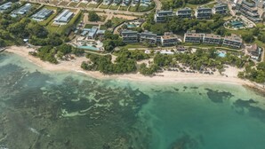 Vista aérea de um hotel à beira-mar, com vários edifícios, uma praia e águas cristalinas.