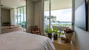 Quarto de hotel moderno com uma cama grande, varanda com vista, televisão e uma pequena mesa com cadeiras.