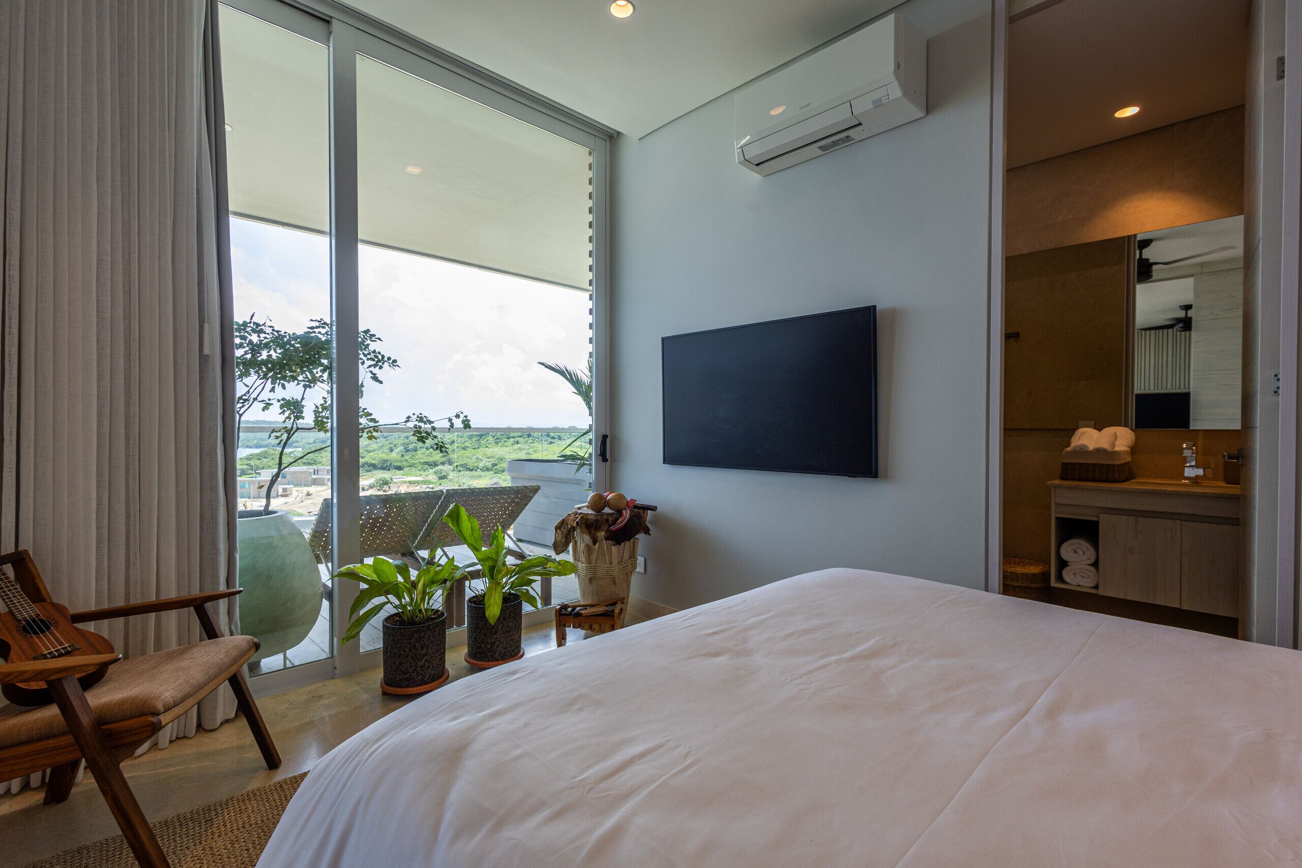 Ein modernes Hotelzimmer mit einem großen Bett, einem an der Wand befestigten Fernseher, einem Balkon mit Aussicht und einem Holzstuhl.