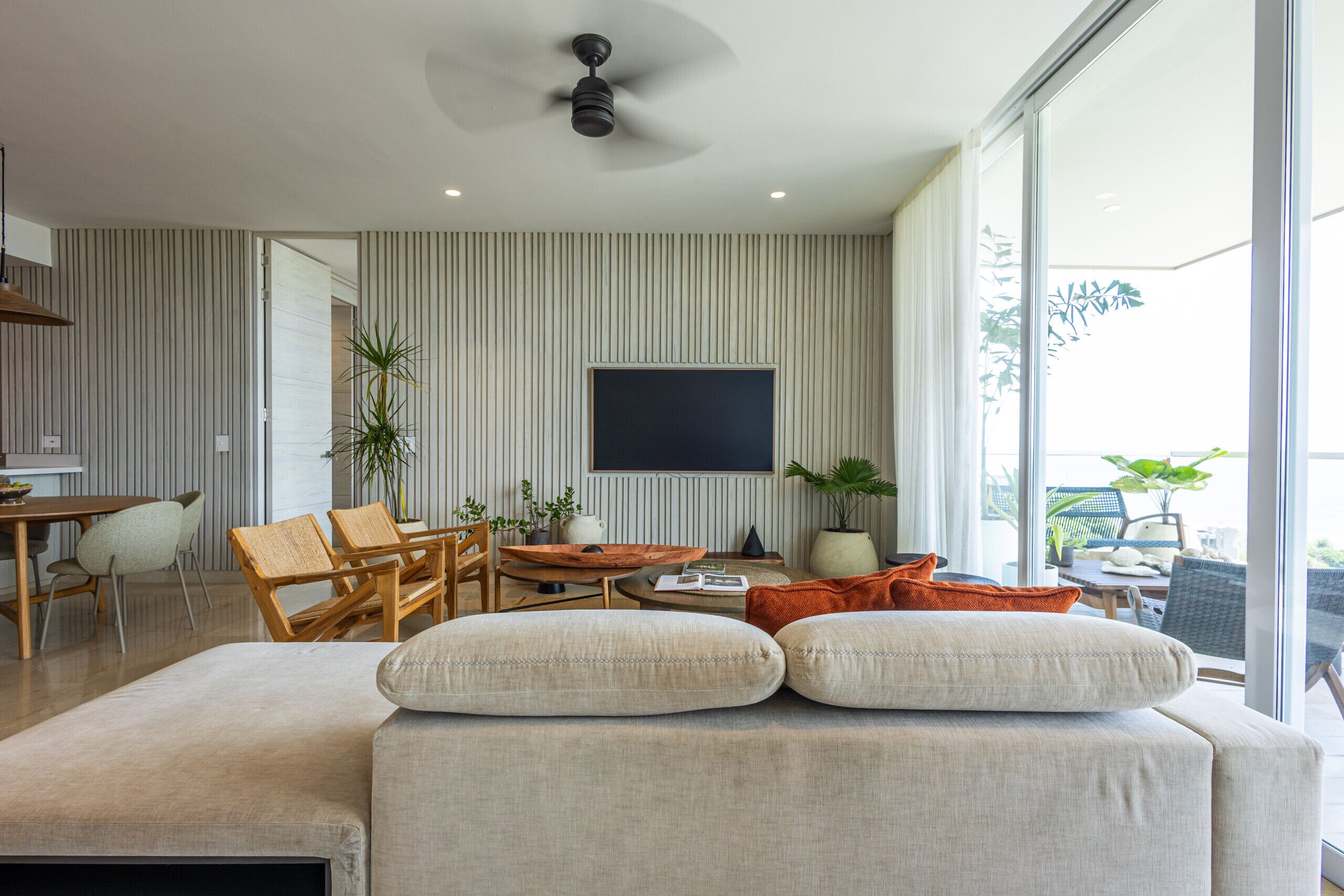 A modern living room with a sofa, a dining area, and a TV mounted on the wall.