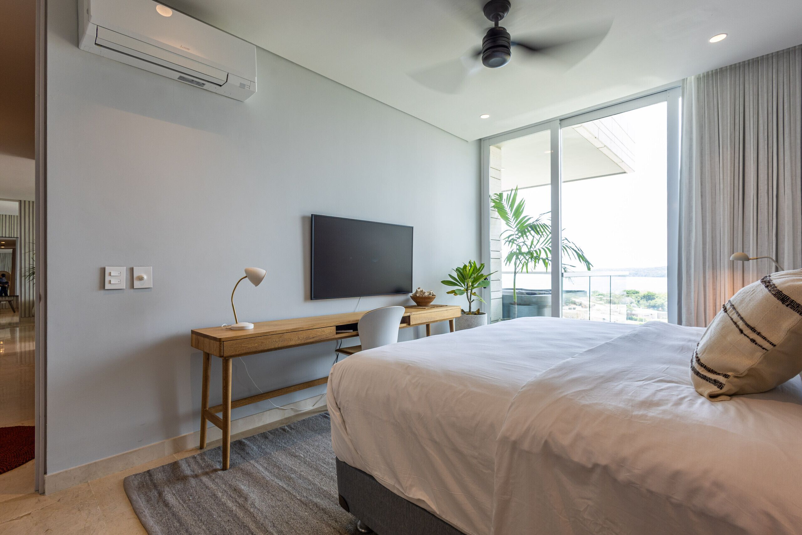 Une chambre d’hôtel moderne dotée d’un grand lit, d’un bureau avec un téléviseur à écran plat, d’un ventilateur de plafond et d’un balcon avec vue.