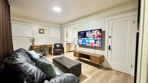 Una sala de estar con un sofá de cuero, una mesa de centro de madera, un televisor montado en la pared y una puerta a la derecha.