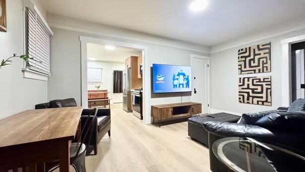 Una sala de estar moderna con una mesa de comedor de madera, un sofá de cuero negro y un televisor de pantalla plana montado en la pared.