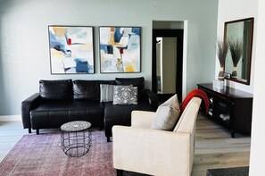 Een moderne woonkamer met een zwarte leren bank, een witte fauteuil, een salontafel en abstracte schilderijen aan de muur.
