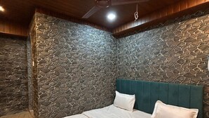 Une chambre avec un mur en pierre, un lit avec une literie blanche et un ventilateur de plafond.