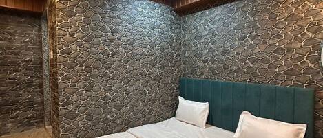 A bedroom with a stone wall, a bed with white bedding, and a ceiling fan.