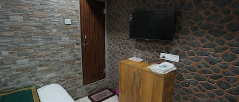 A room with a stone wall, a wooden door, a bed with a green and white bedspread, a wooden cabinet, and a flat-screen TV mounted on the wall.