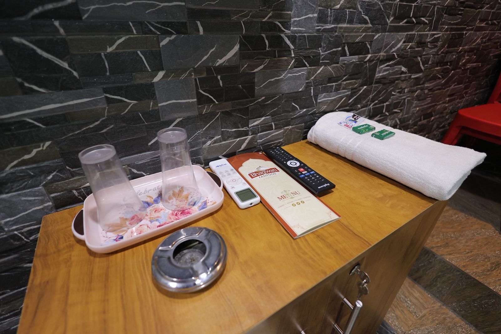 A wooden table with a towel, a remote control, a menu, and a glass container with a floral design.