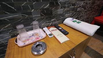 A wooden table with a towel, a remote control, a menu, and a glass container with a floral design.