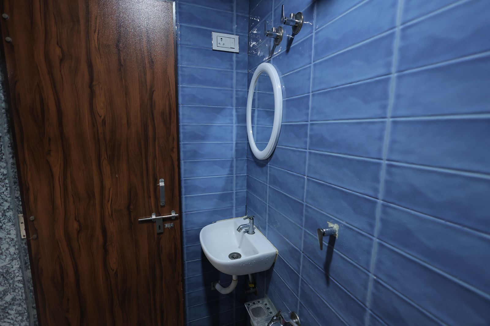 Ein Badezimmer mit blauen Fliesenwänden, einer Holztür, einem weißen Waschbecken und einer Toilette.