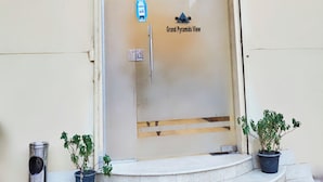A hotel entrance with a glass door, a sign reading "Grand Pyramids View," and two potted plants on the steps. - The Great Golden Pyramid (Giza)