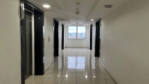 A hallway with a view of a cityscape through large windows, leading to an elevator and a door. - Apartment Bassura City By Berkah Estate By Zuzu (Jakarta)