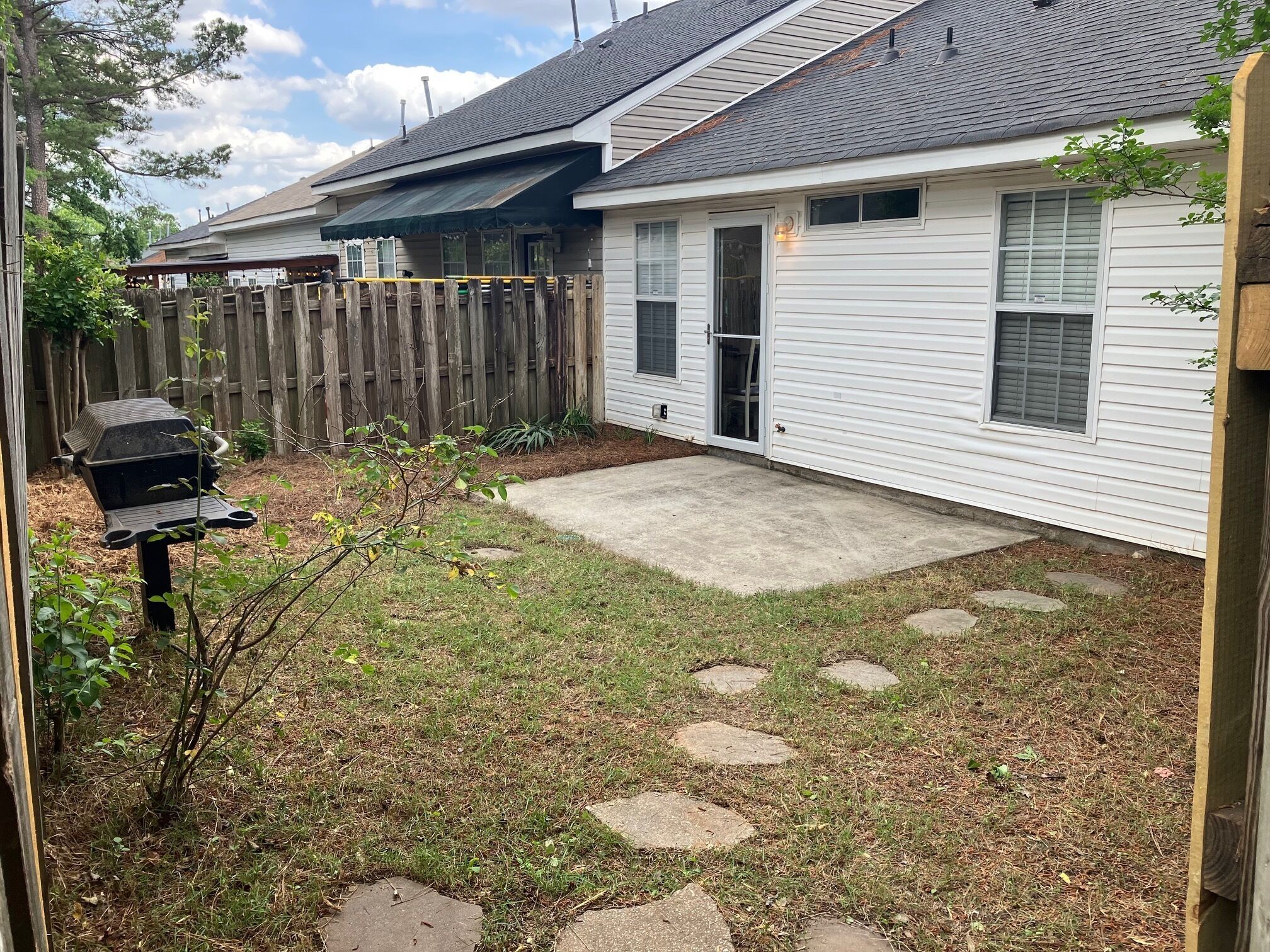 A residential backyard with a concrete patio, a wooden fence, and a barbecue grill.
