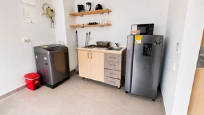 Eine kompakte Küchenzeile mit Kühlschrank, kleinem Herd, Spüle und Mülleimer.