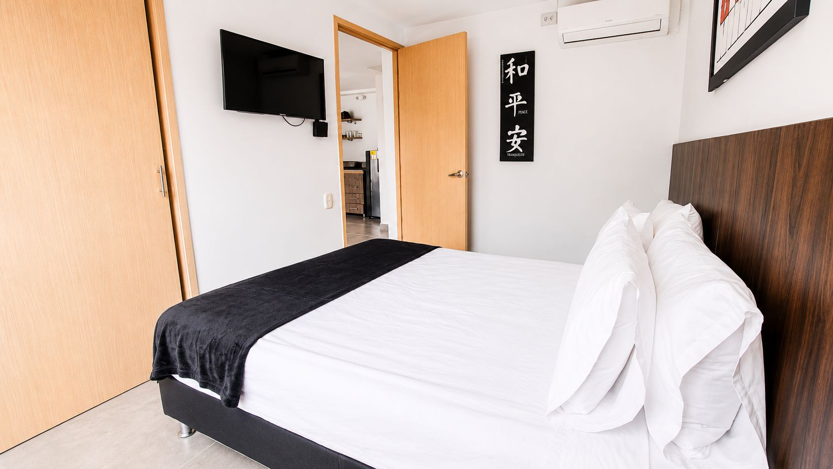 Ein Schlafzimmer mit einem Bett, einem an der Wand befestigten Fernseher, einer Holztür und einem Schild mit japanischen Schriftzeichen.