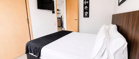 A bedroom with a bed, a television mounted on the wall, a wooden door, and a sign with Japanese characters.