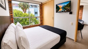 Een hotelkamer met een bed, een aan de muur bevestigde televisie en een raam met uitzicht op bomen en gebouwen.