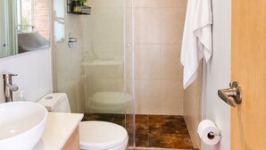 Een moderne badkamer met een douche met glazen wand, een wit toilet, een wastafel en een rode prullenbak.