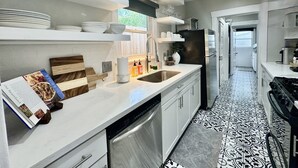 A modern kitchen with white cabinetry, a stainless steel dishwasher, and a black refrigerator. - Cozy Houston Retreat • Private Gated | Holly House (Houston)