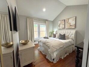 Une chambre à coucher avec un grand lit, une table de chevet, un miroir et une fenêtre avec des rideaux.