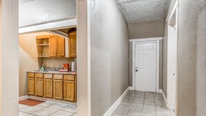 A narrow hallway with a white door at the end, tiled floor, and wooden cabinets in the adjacent kitchen area. - Urban Comfort Nook - Walk to Overton Park (Memphis)