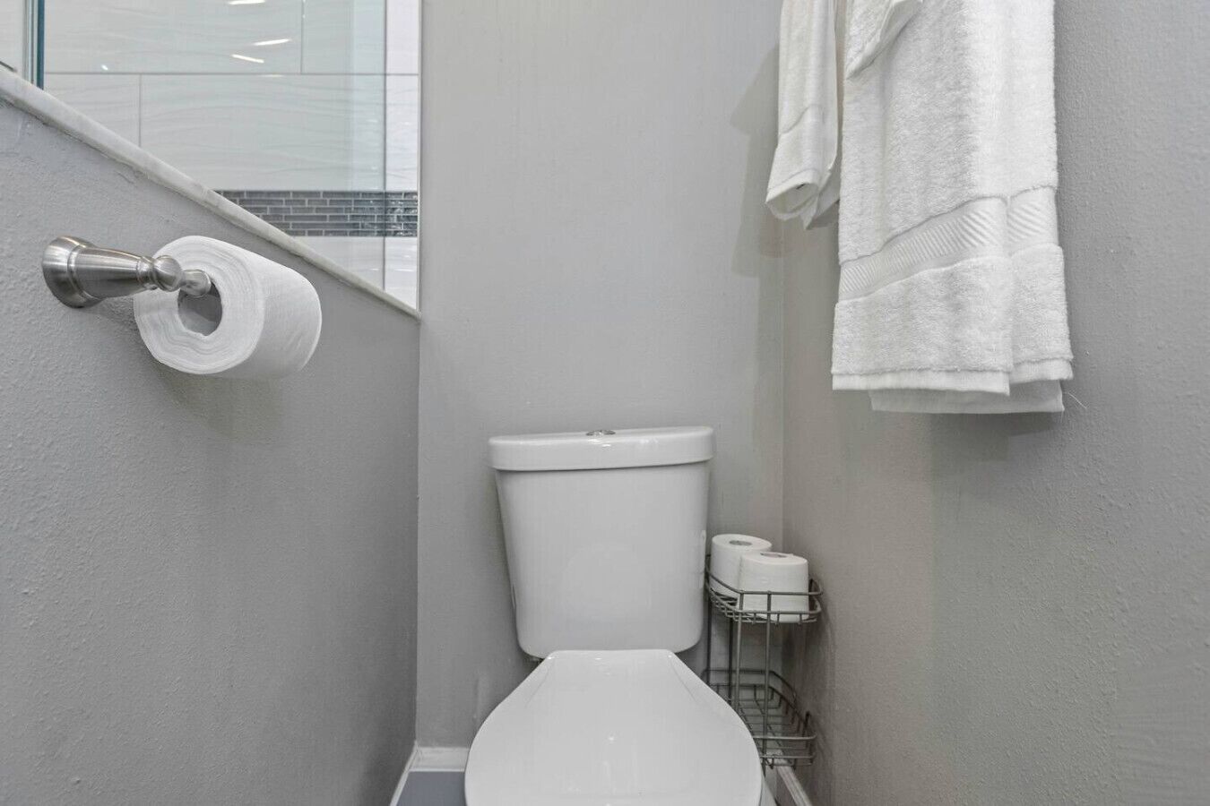 A small, modern bathroom with a toilet, a roll of toilet paper, and a towel rack with towels.