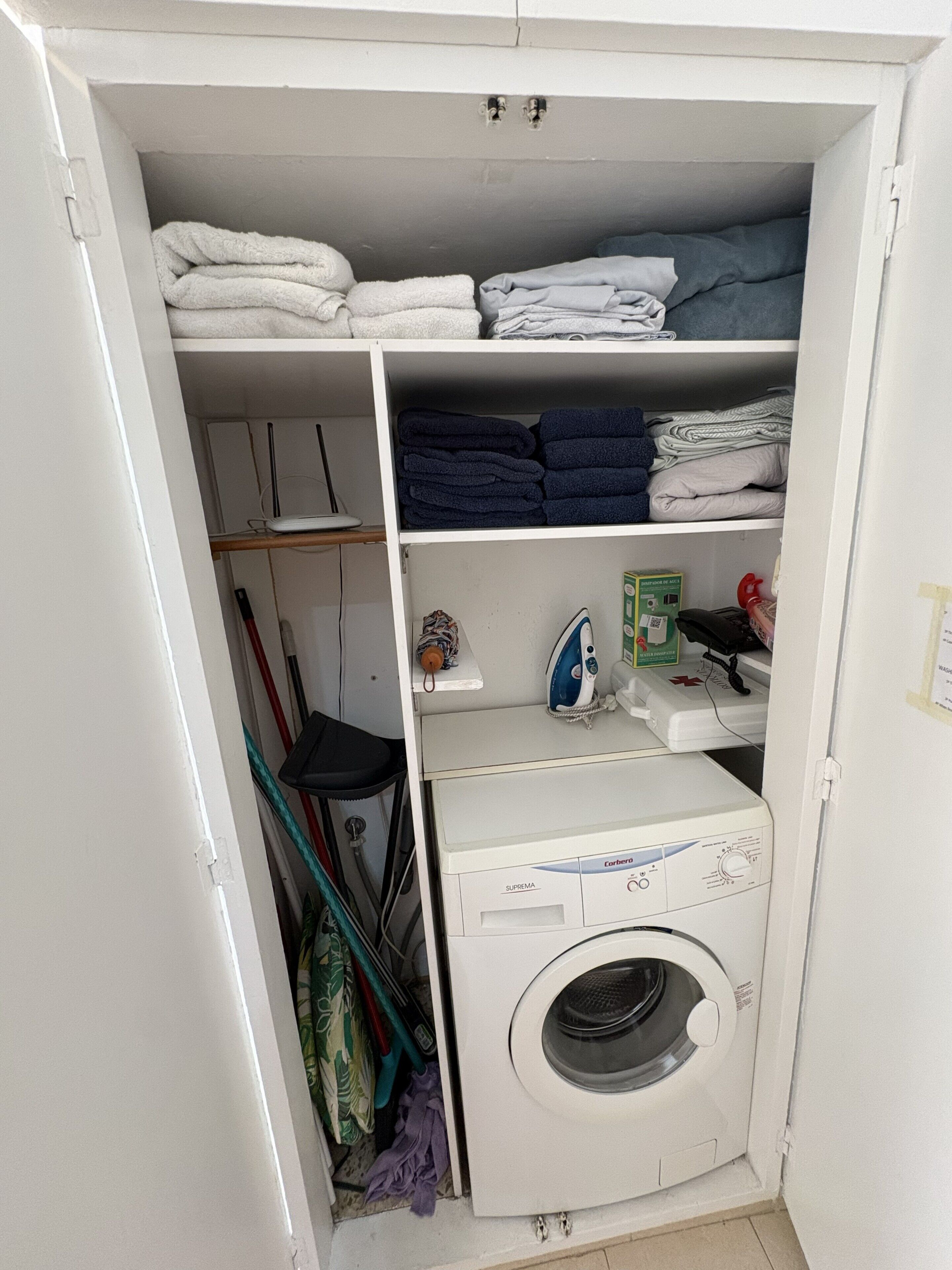 A laundry room with a washing machine, shelves with folded towels, and cleaning supplies.
