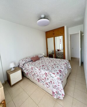 A bedroom with a bed, nightstand, lamp, wardrobe, and a ceiling fan.