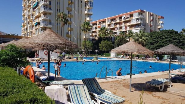 Piscina com espreguiçadeiras e guarda-sóis, cercada por edifícios altos.