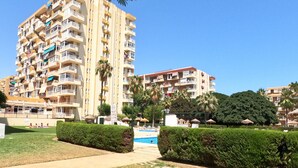 Um edifício residencial de vários andares com varandas, piscina e jardins bem cuidados.