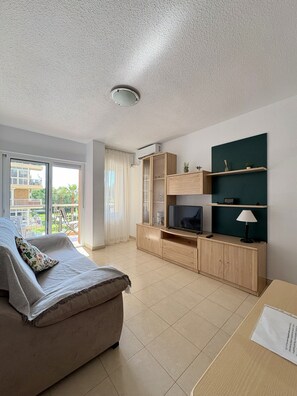 A modern living room with a sofa, TV stand, and a balcony view.