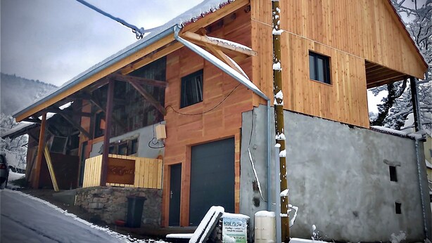 A wooden cabin with a sloped roof, a large window, and a stone foundation. - The Munster valley stable (Breitenbach-Haut-Rhin)