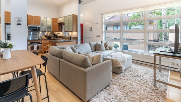 A modern kitchen with stainless steel appliances, a dining area with a wooden table and chairs, and a large window with a view of the outside. - Mountain Retreat in East Vail, 2BR/2BA Condo w/ Pool & Hot Tub (Vail)